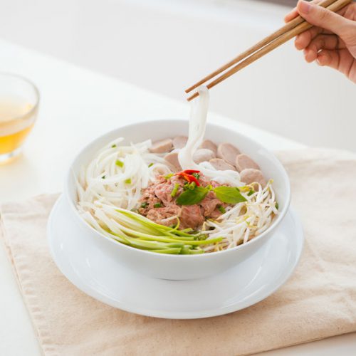 Woman eating traditional Vietnamese Pho noodle using chopsticks.